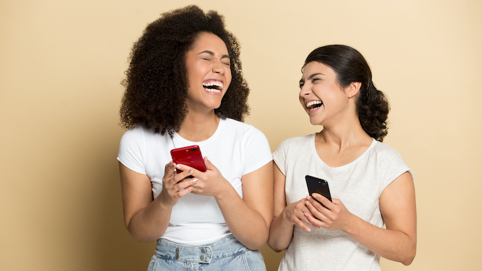 Two young woman on their phones laughing at a joke