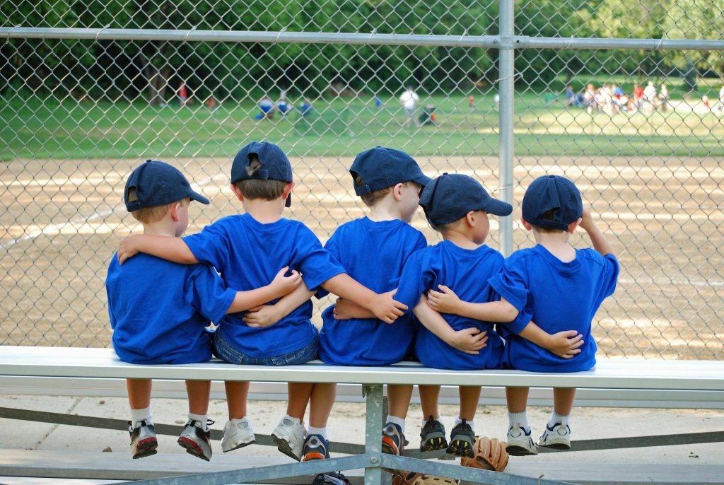 Little kids hugging in front of a baseball field